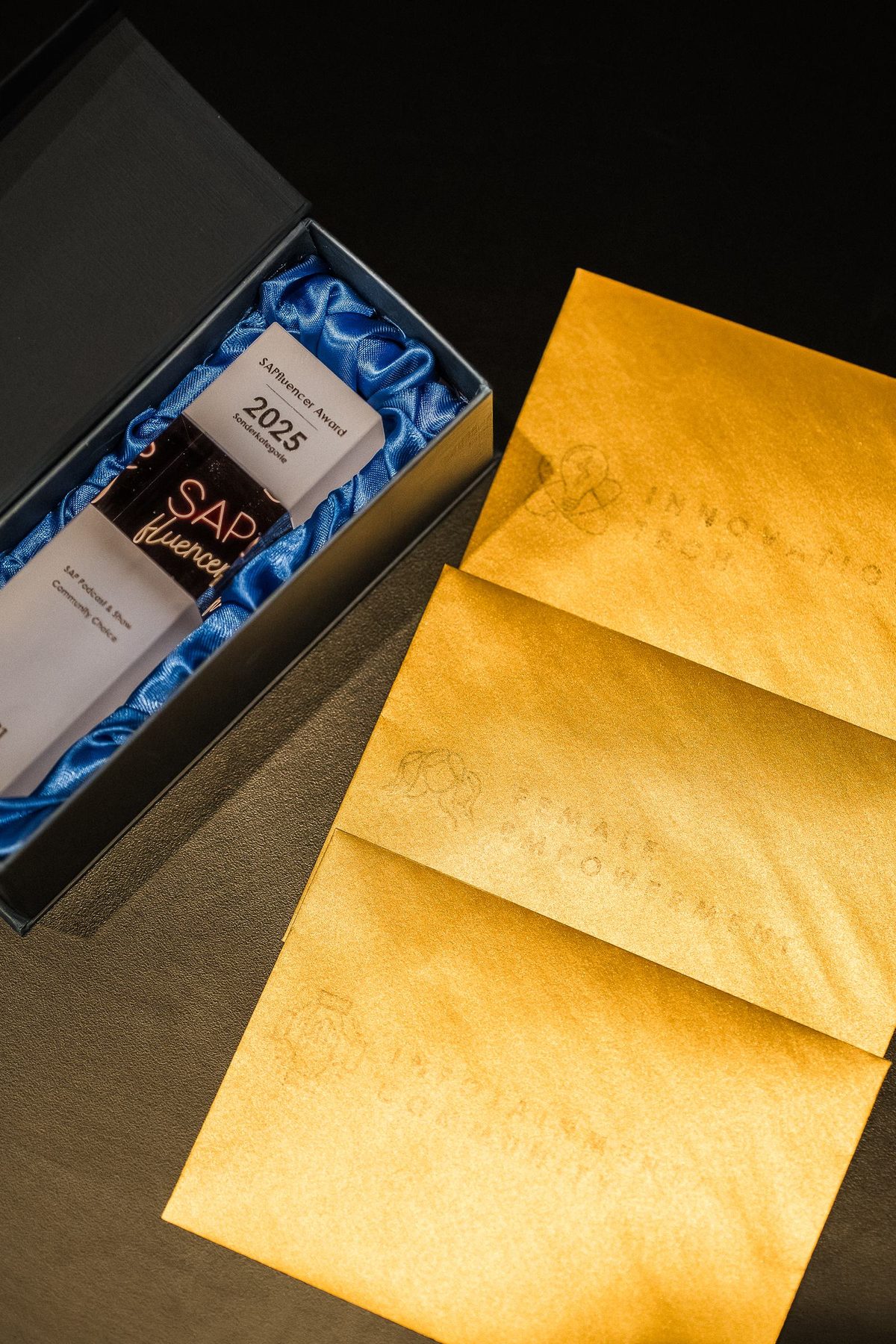 Trophäe der Sonderkategorie in der Box, daneben goldene Umschläge
